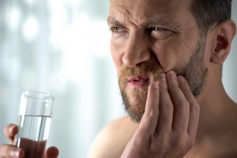 A man experiencing tooth hypersensitivity while rinsing the mouth with water